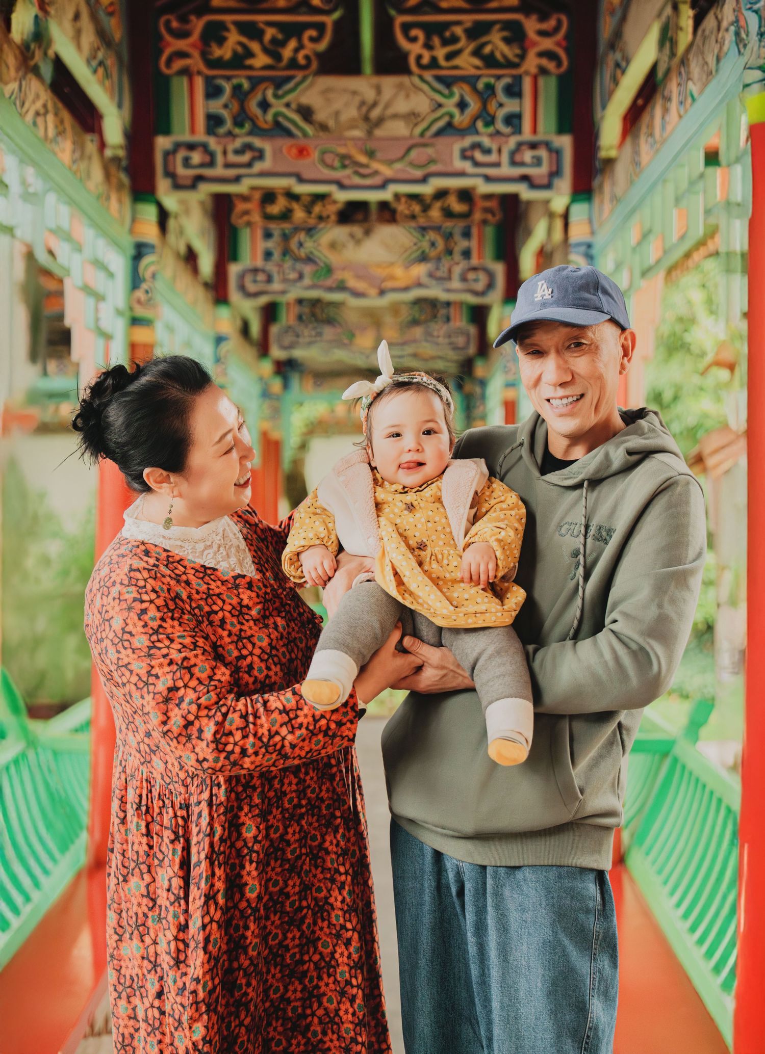 Grandparents smiling and holding a baby girl in a colorful Chinese corridor.