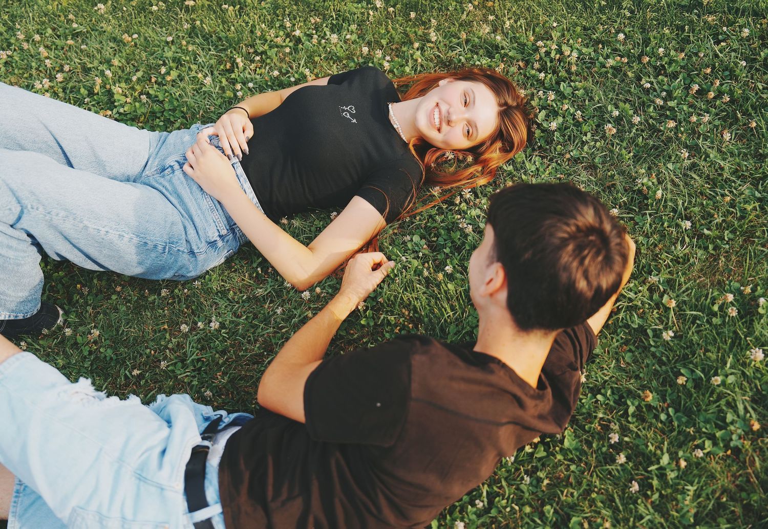 Young couple relaxing on green grass laughing together on a sunny day outdoors.