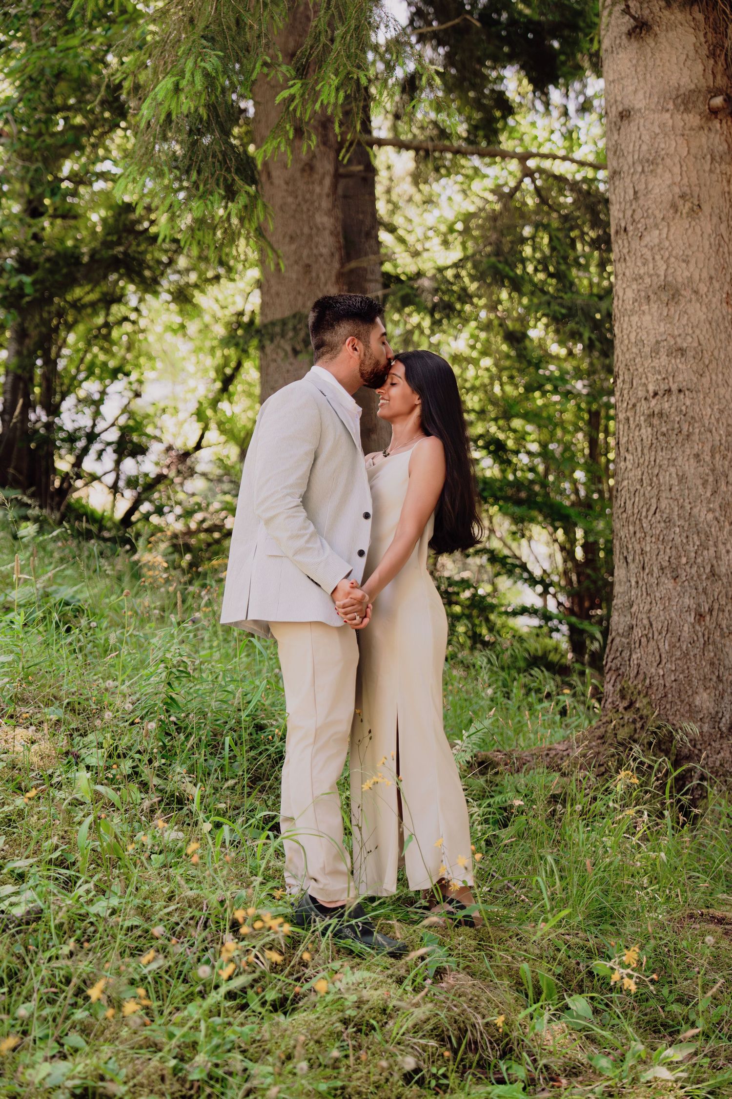 Romantic couple embracing tenderly under tall trees in a lush green Swiss forest setting.