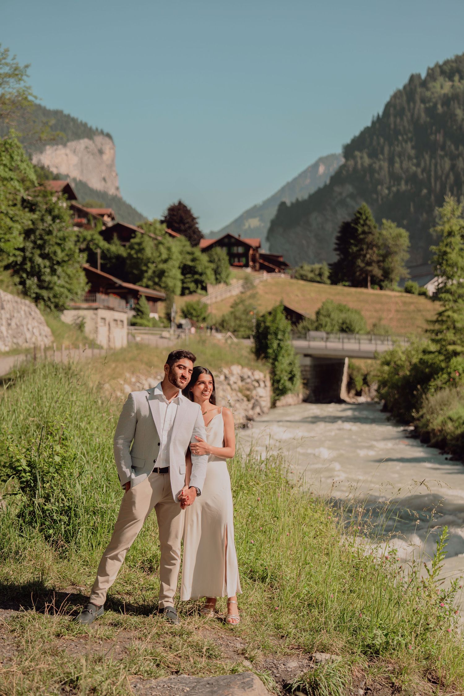 Elegant couple posing near a rushing stream with mountain scenery in Switzerland.