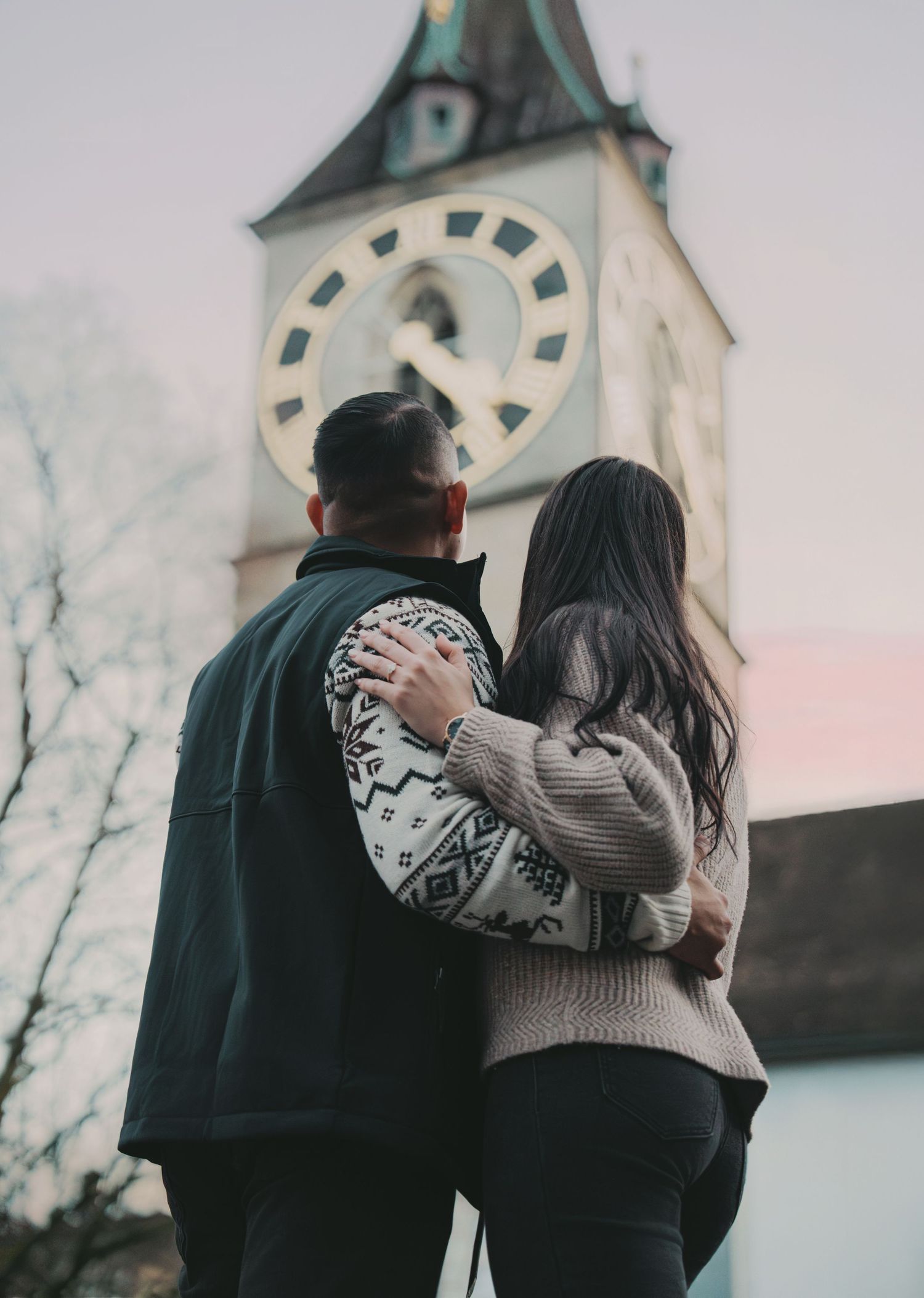 Couple embracing while admiring a historic clock tower at dusk in Zurich, Switzerland.