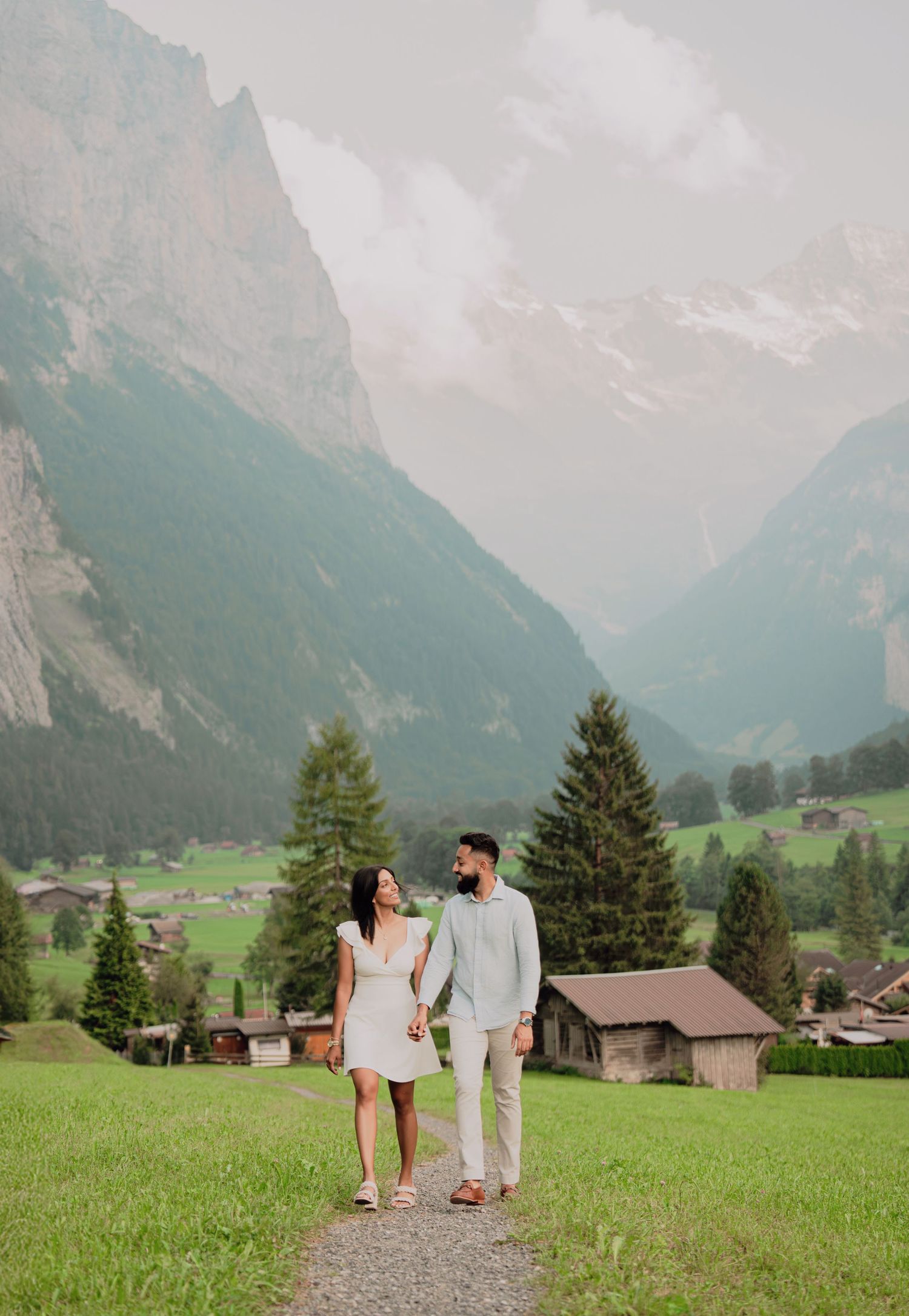 Smiling couple holding hands and walking together on a mountain path in a picturesque Swiss valley.
