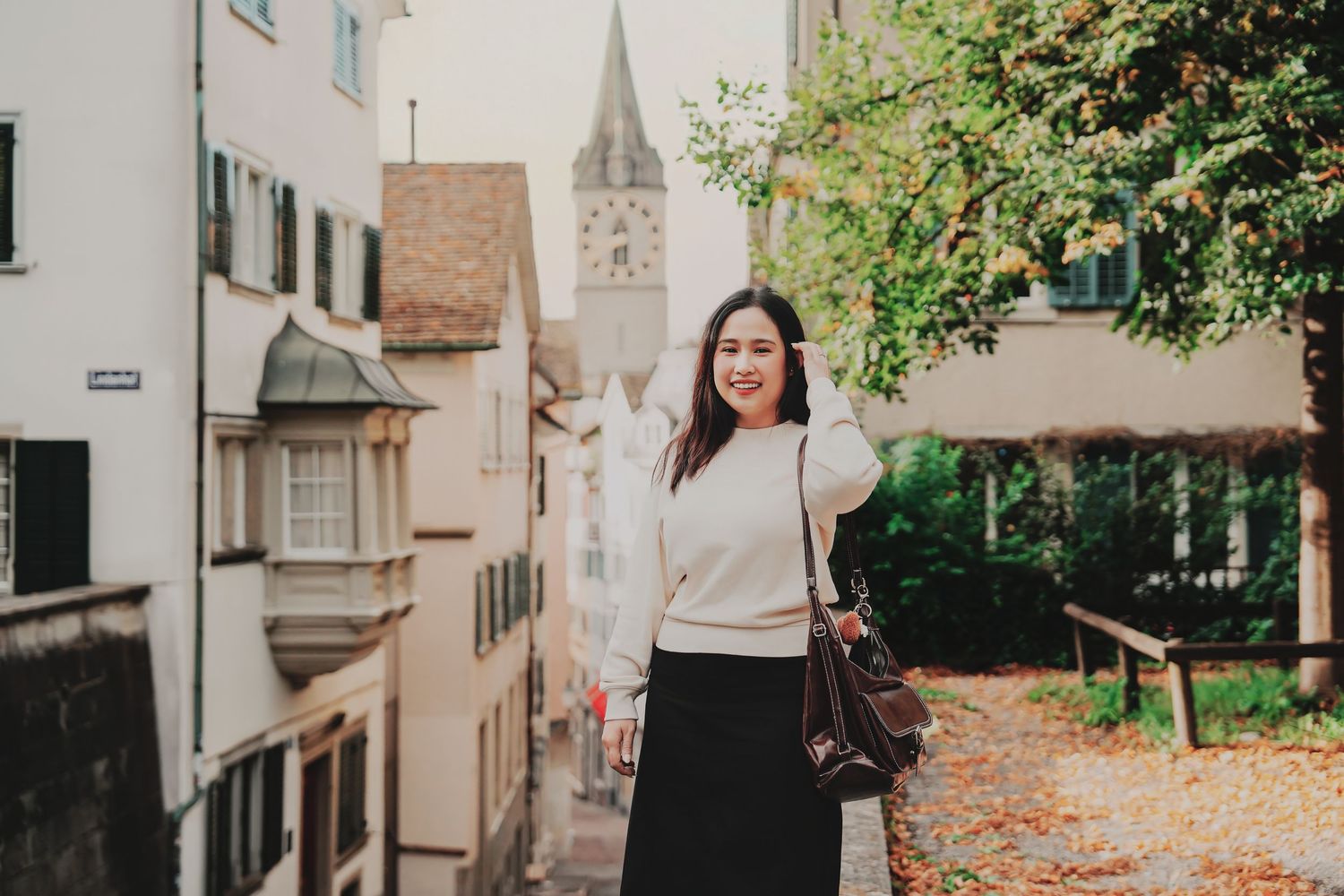 Smiling Asian woman posing on a charming Swiss street with a historic church tower visible in background.