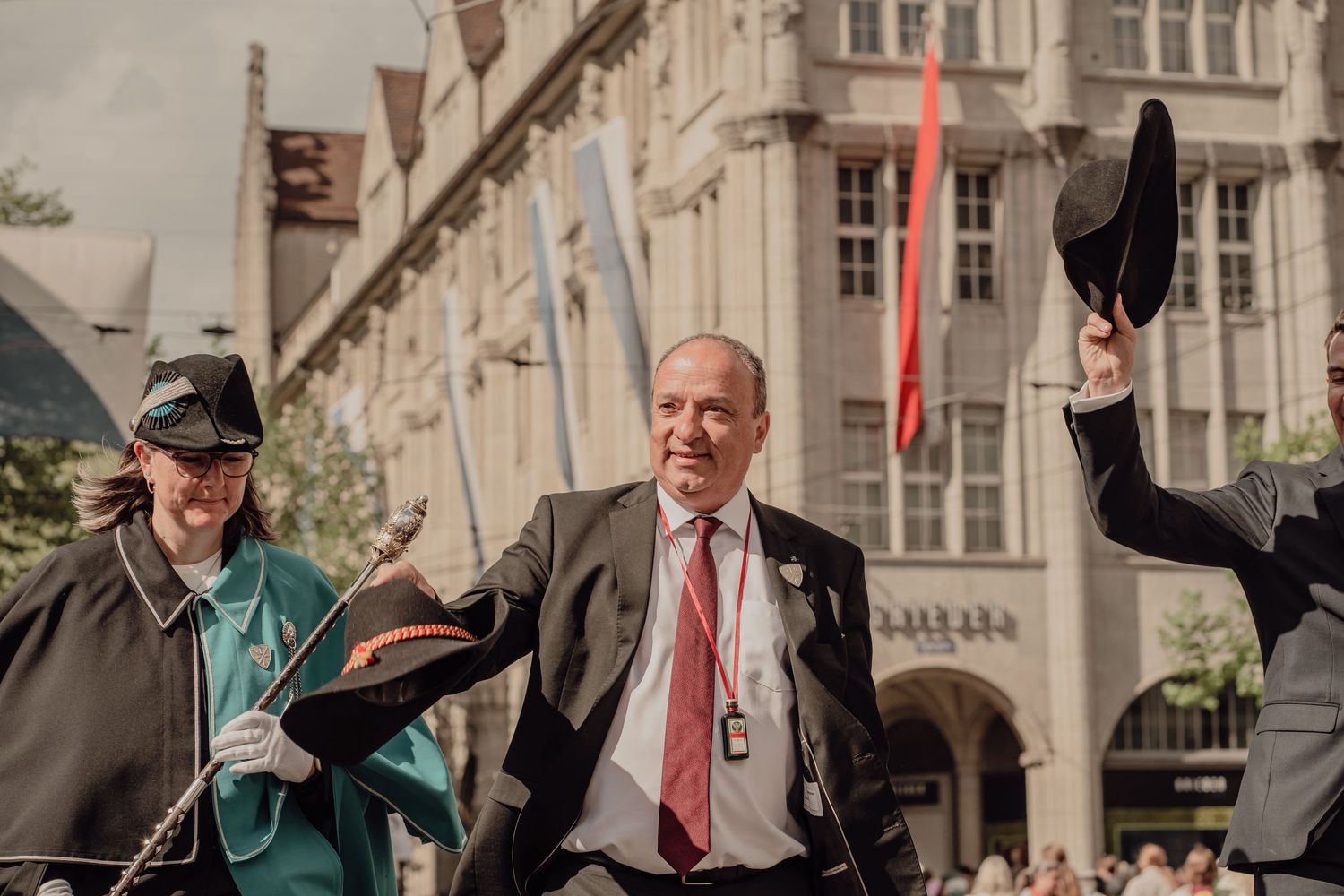 Three people in historical costumes tip their hats joyfully during a festive outdoor parade celebration.