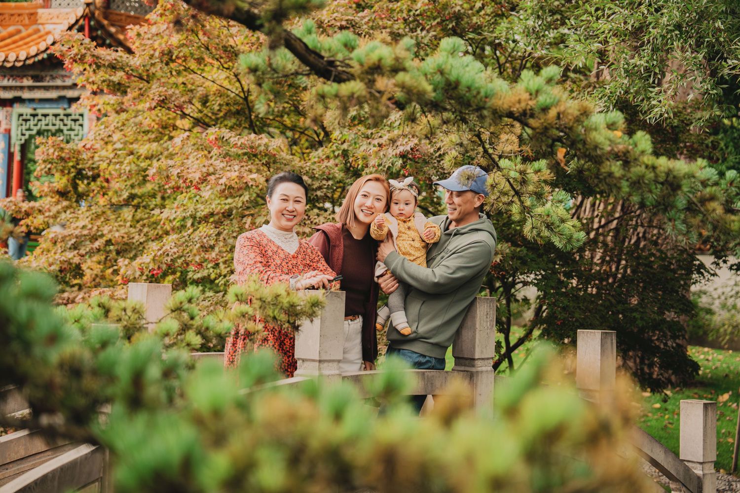 Family of four posing together in a Chinese garden with colorful autumn foliage and traditional architecture.