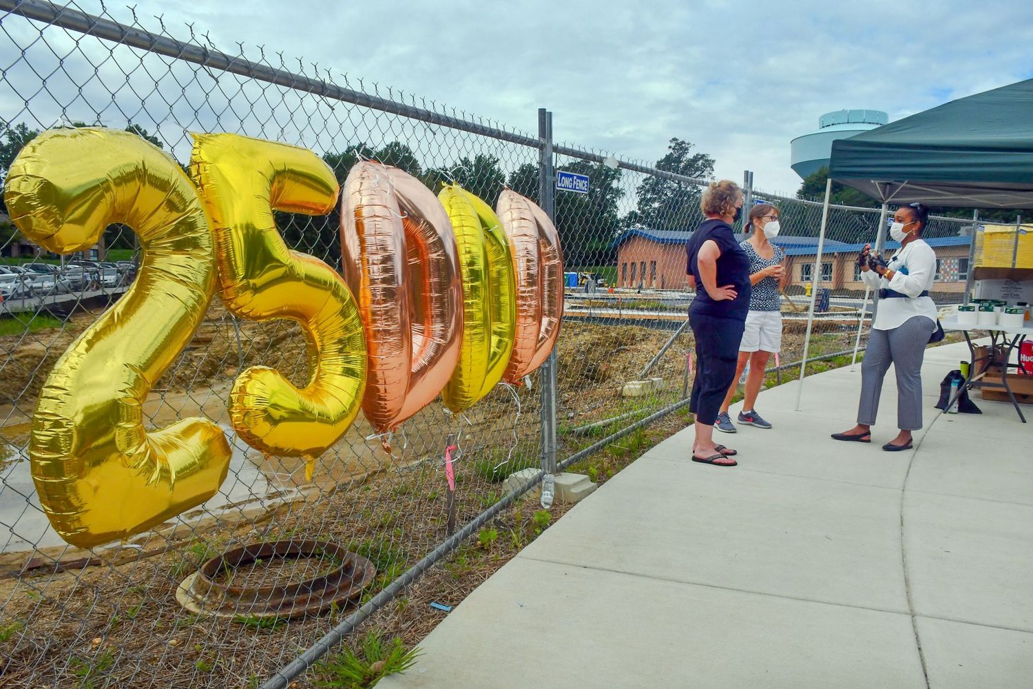 Colorful balloons and tents set up along a fence at an outdoor community event.