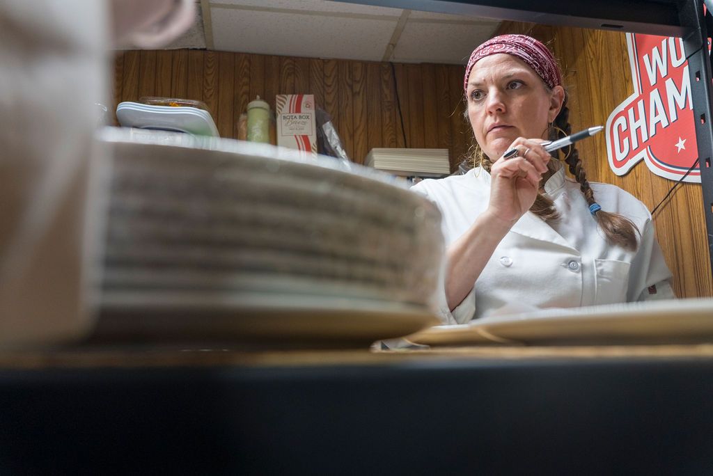 Restaurant workers preparing food in kitchen with wooden paneled walls.