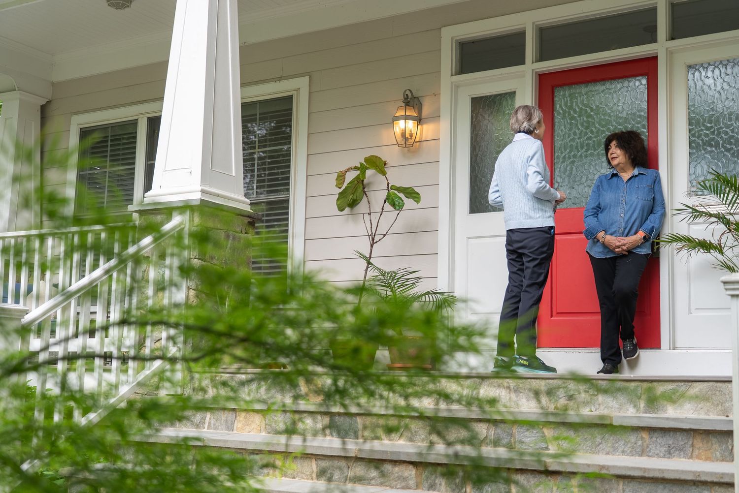 Two people conversing on a charming home front porch with a red door and white siding.