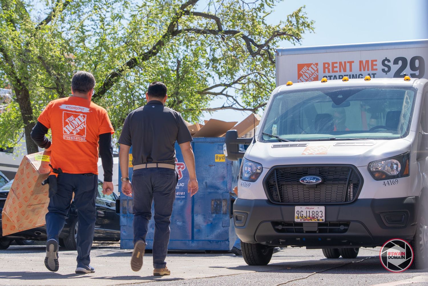 A row of rental moving trucks and vans parked in a line at a rental facility on a sunny day.