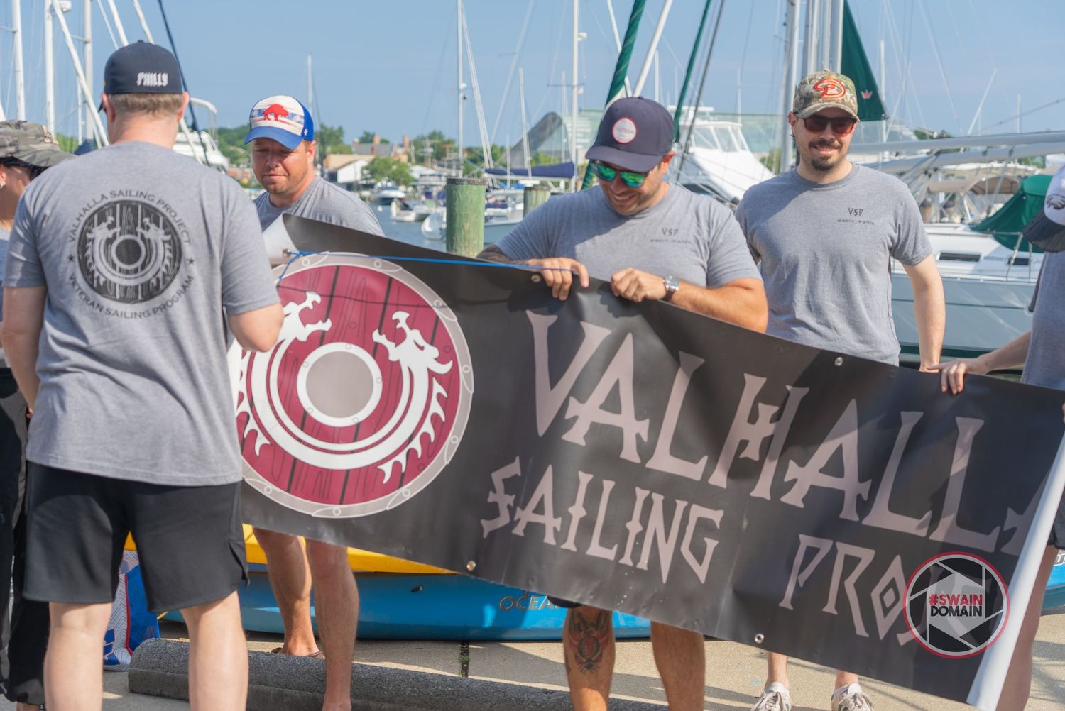 People enjoying beverages at a casual outdoor brewery event with boats and water in the background.
