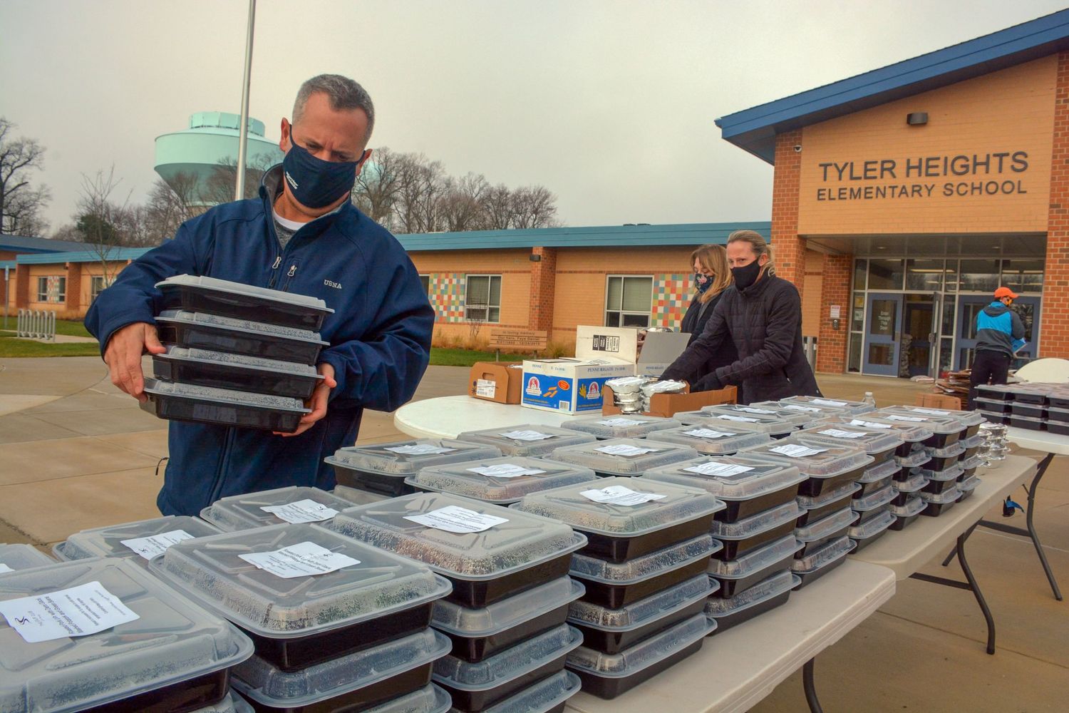 Volunteers arranging stacks of prepared meal containers on folding tables outside.