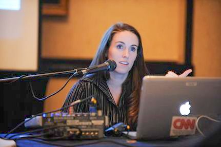Speaker presenting at podium with laptop and microphone setup in conference room.
