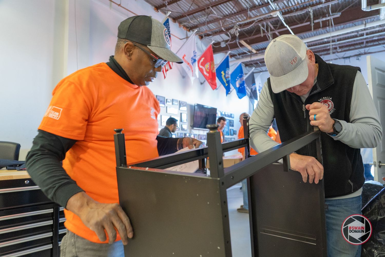 A person in an orange safety vest works on installing equipment in an industrial warehouse setting.