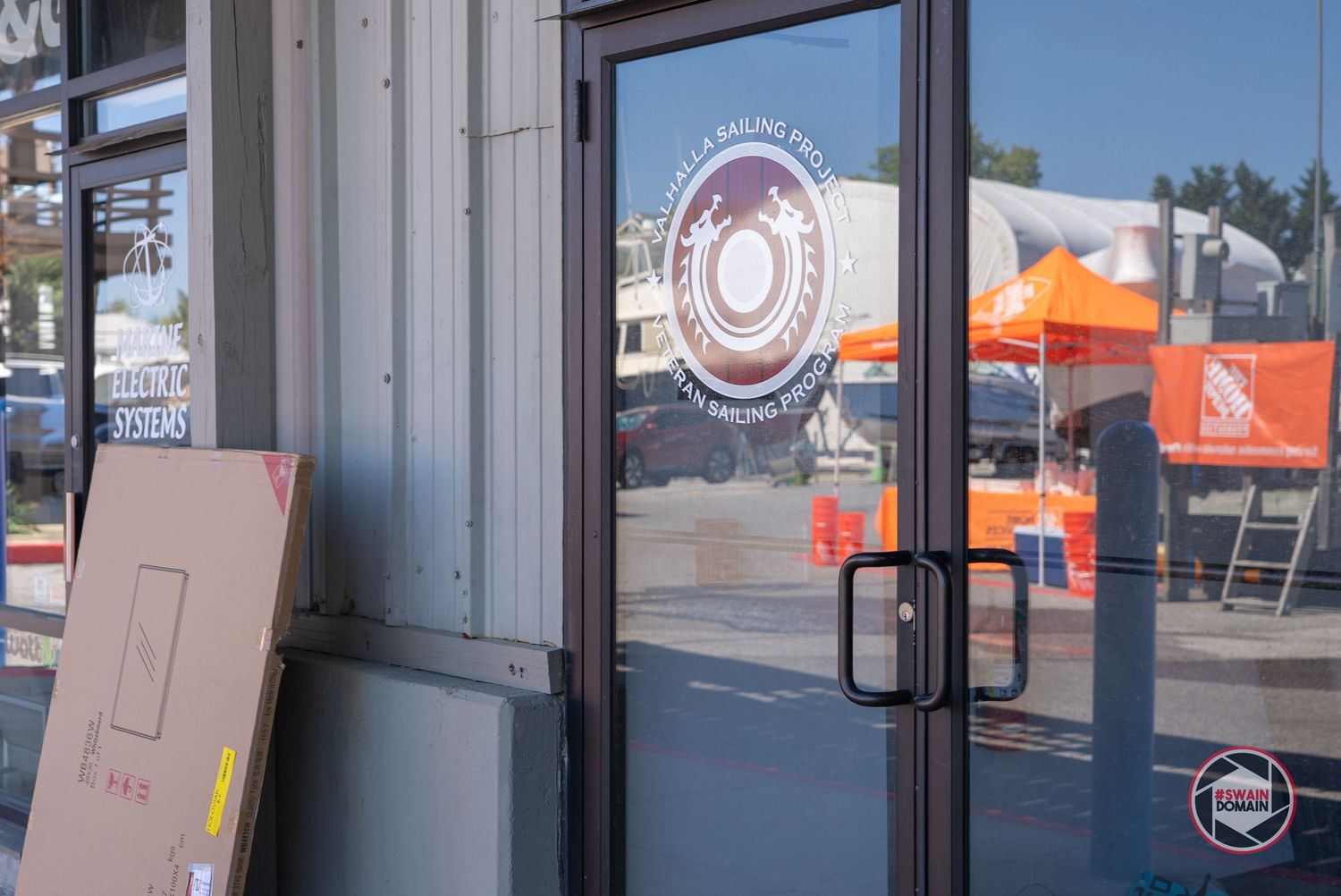 A modern storefront with glass doors and windows displays a business logo and orange signage in daylight.