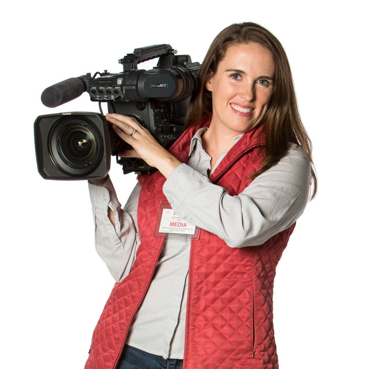 Videographer wearing a red quilted vest holding a professional camera.