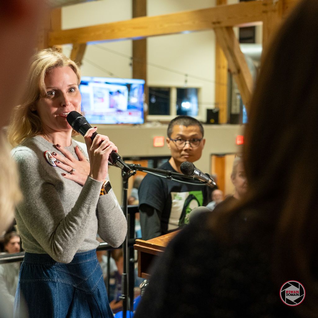 Person speaking into a microphone at a campaign event with audience members listening.