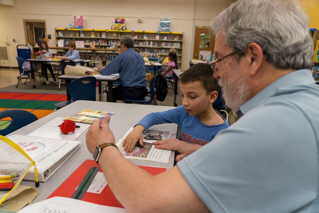 Wide view of a library space showing people working at tables between bookshelves.
