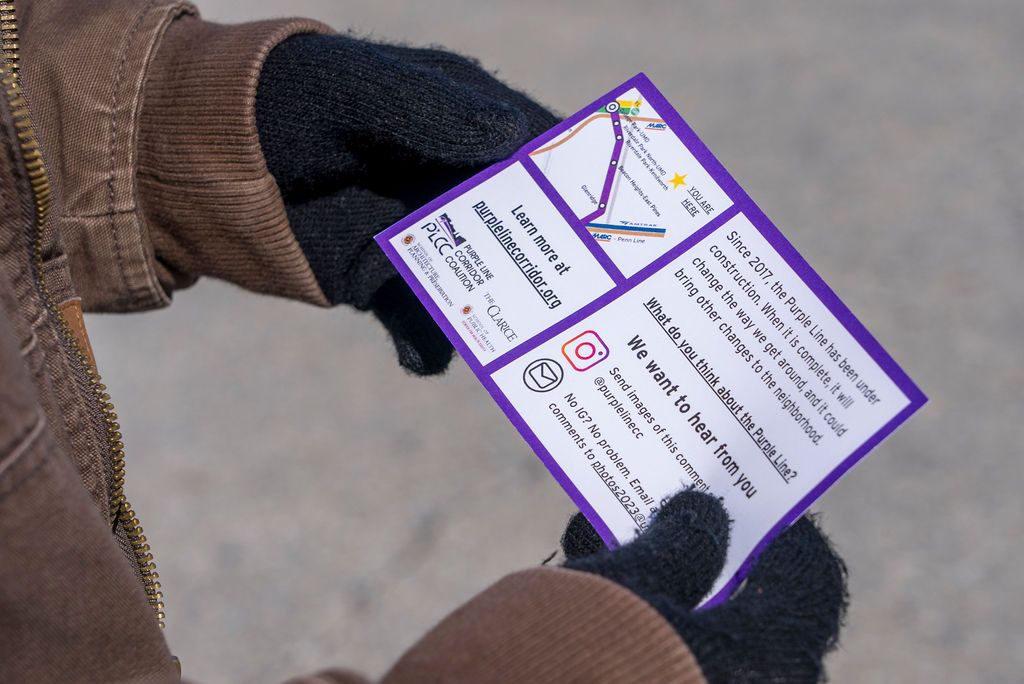 Hands holding purple promotional flyers or documents outdoors.