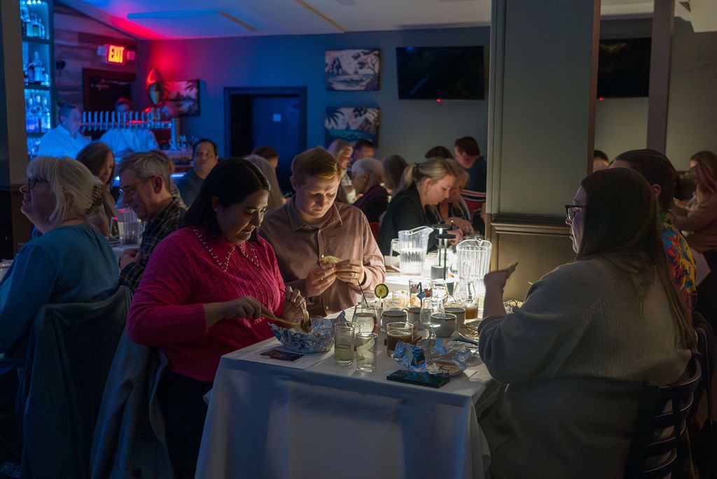 Dimly lit dining room with guests seated at tables under blue and red lighting.