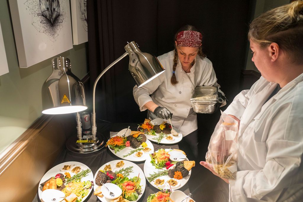 Professional chefs in white coats examining dishes on a counter in a restaurant kitchen.