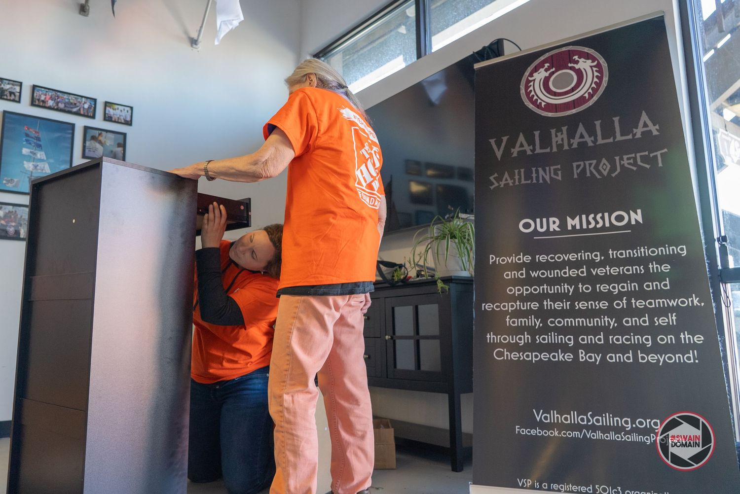 Workers in orange safety vests install wall graphics and signage in an office hallway.