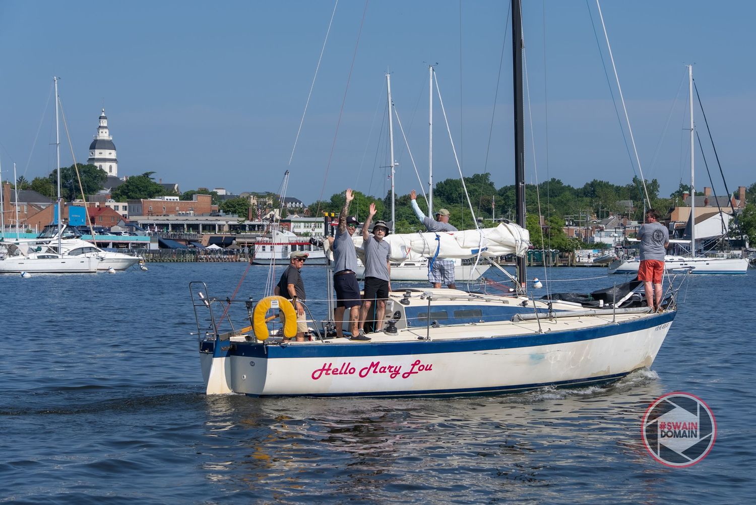 Sailboats and yachts moored in a marina on a sunny day with calm blue waters and distant shoreline.
