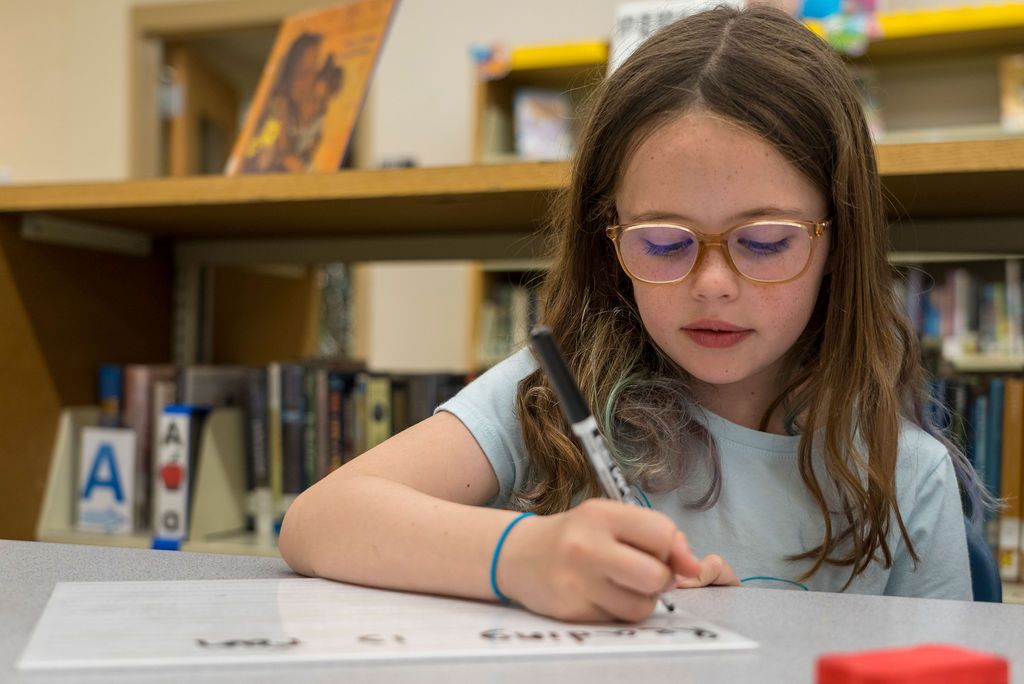 Students focused on reading and writing activities at library tables.