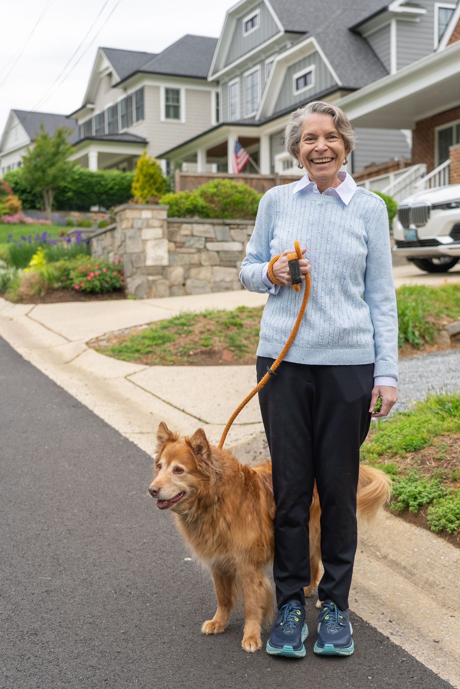 Smiling elderly woman walking a golden dog on a leash in a residential neighborhood street.