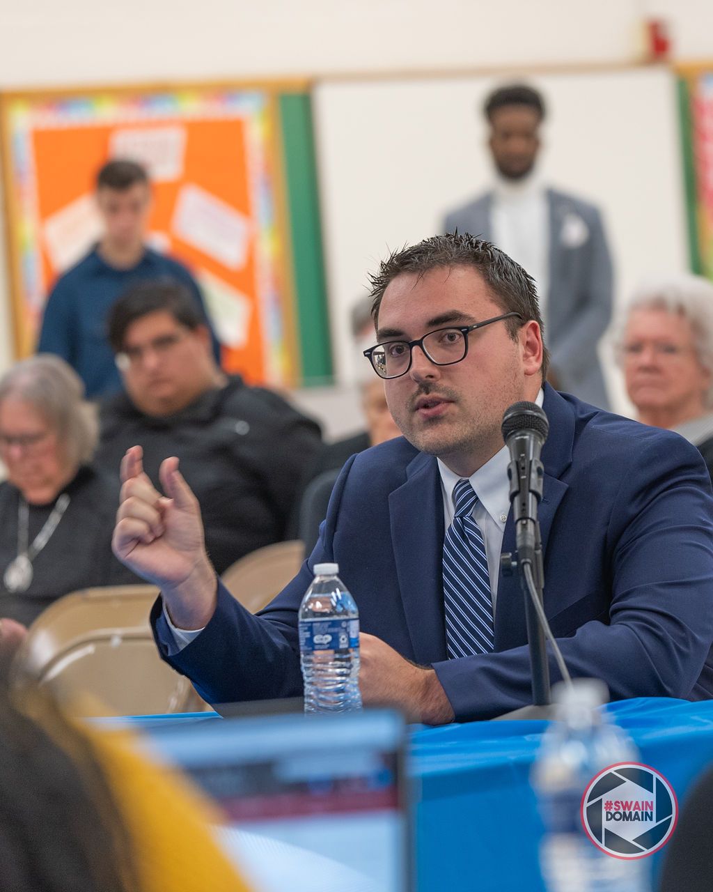 Panel members in business attire discuss topics at a conference table with microphones.