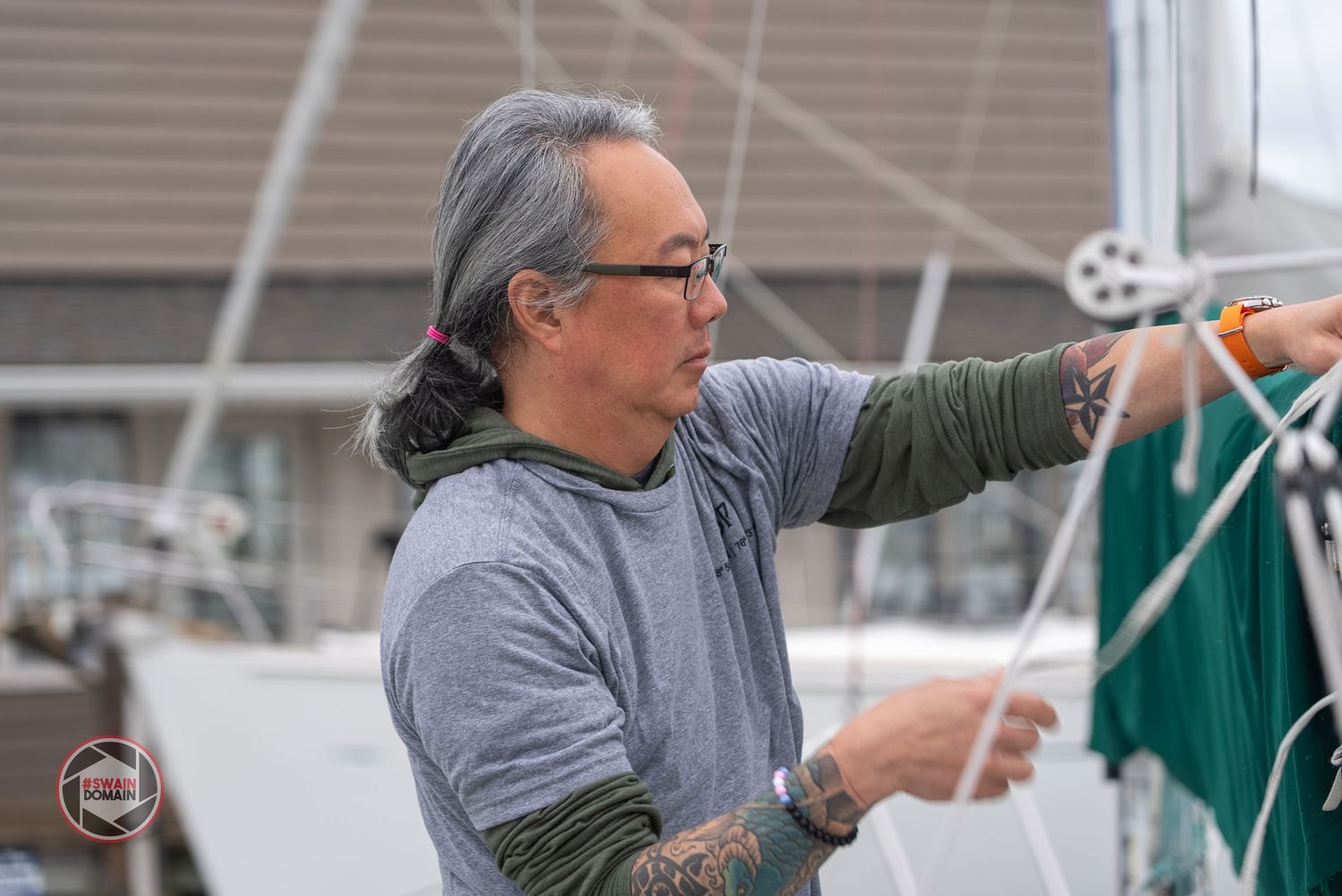 Person in gray sweater adjusts white and green sailing equipment on a boat deck.