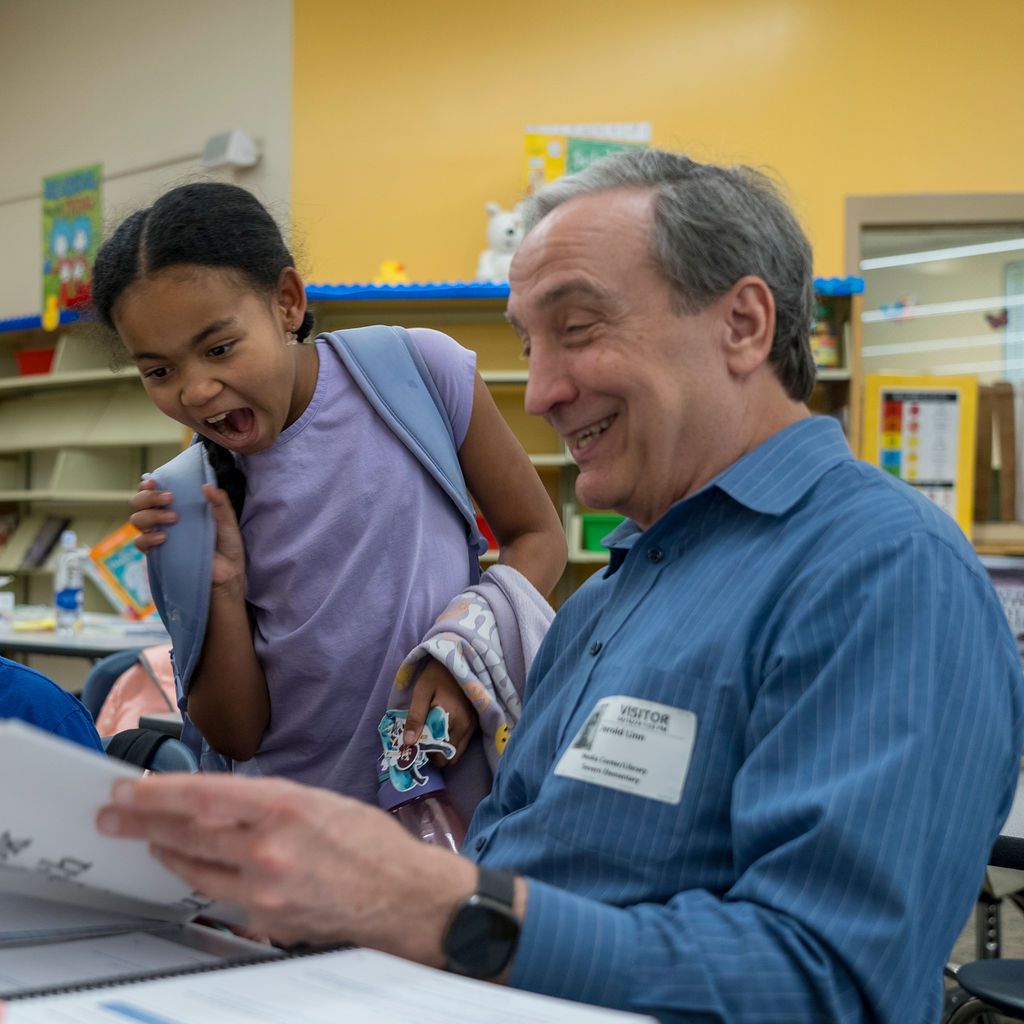 Adults and students working together at tables in a bright yellow-walled library space.