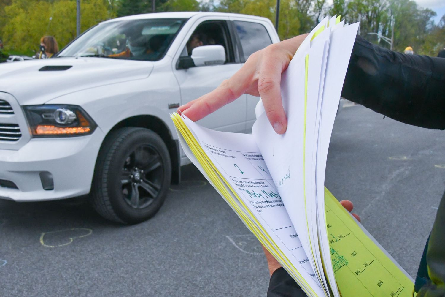 Cars lined up in a parking lot with paperwork being processed at a drive-through event.