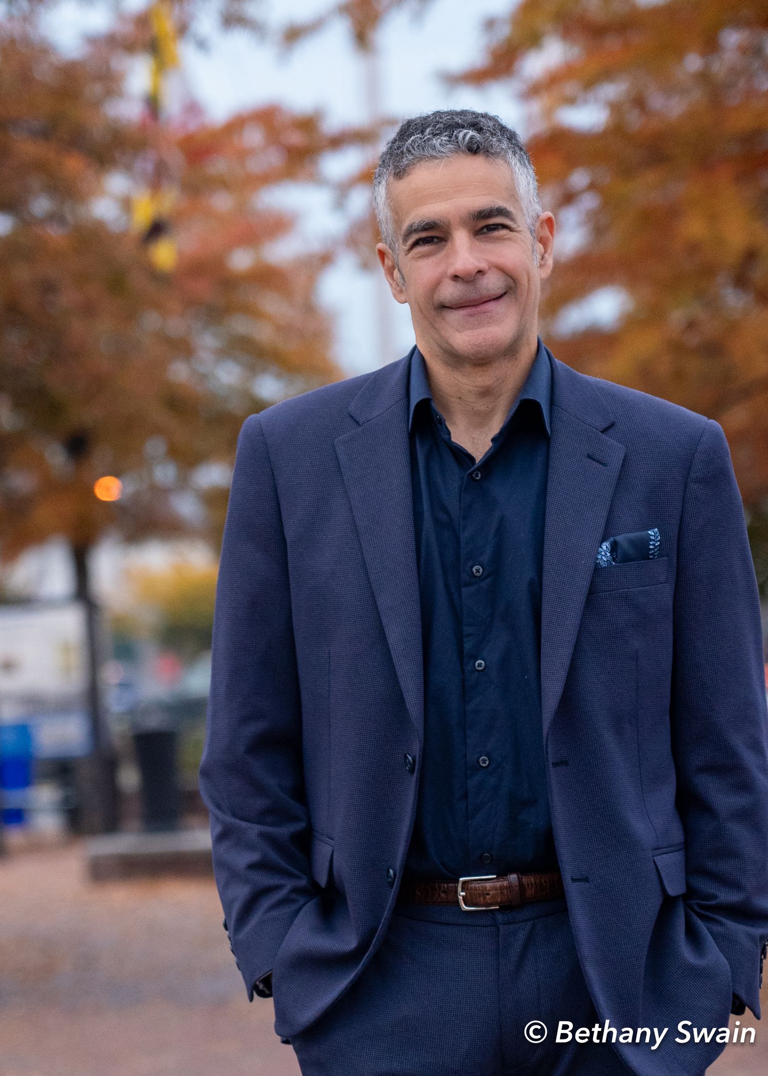 Jared DeMarinis in navy suit stands outdoors among autumn trees.