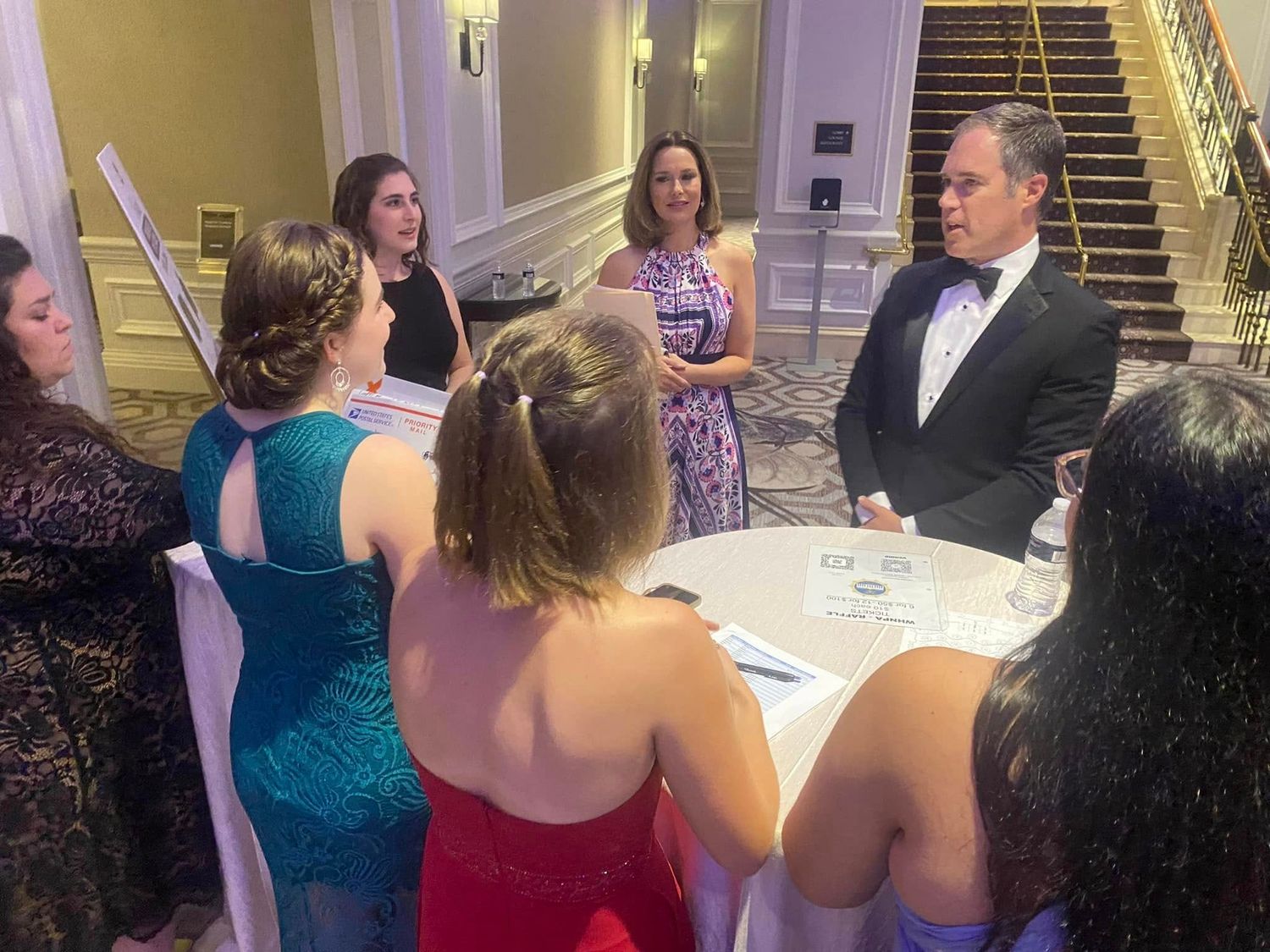 Elegantly dressed guests networking around a table at a formal black-tie gala event.