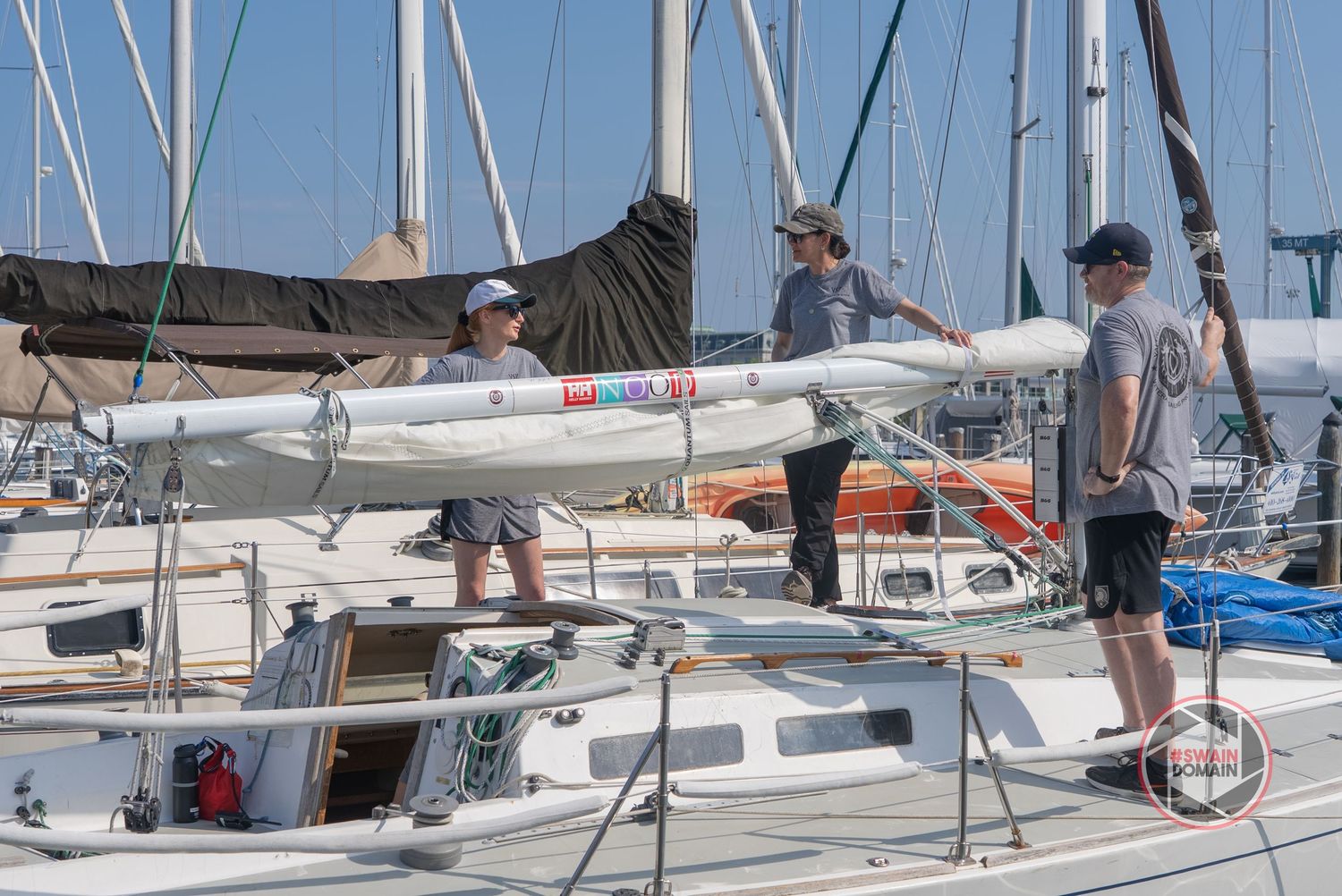 People sailing and learning boat handling techniques on small sailboats in a marina during a sunny day.