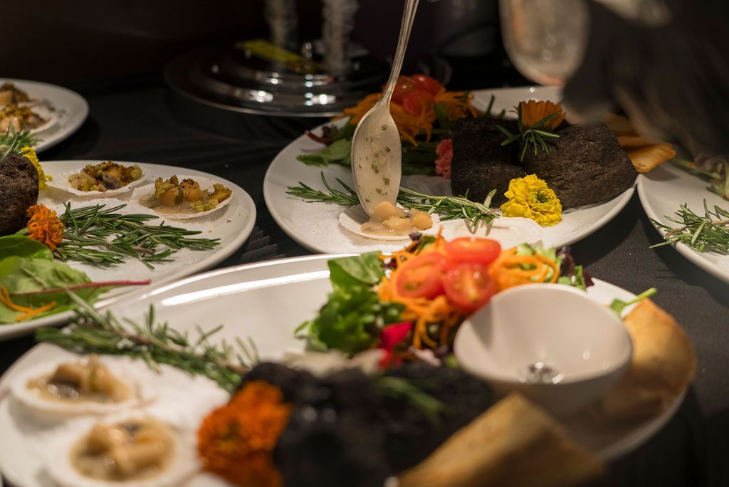 Elegant plated dishes with colorful garnishes arranged on a dark surface.