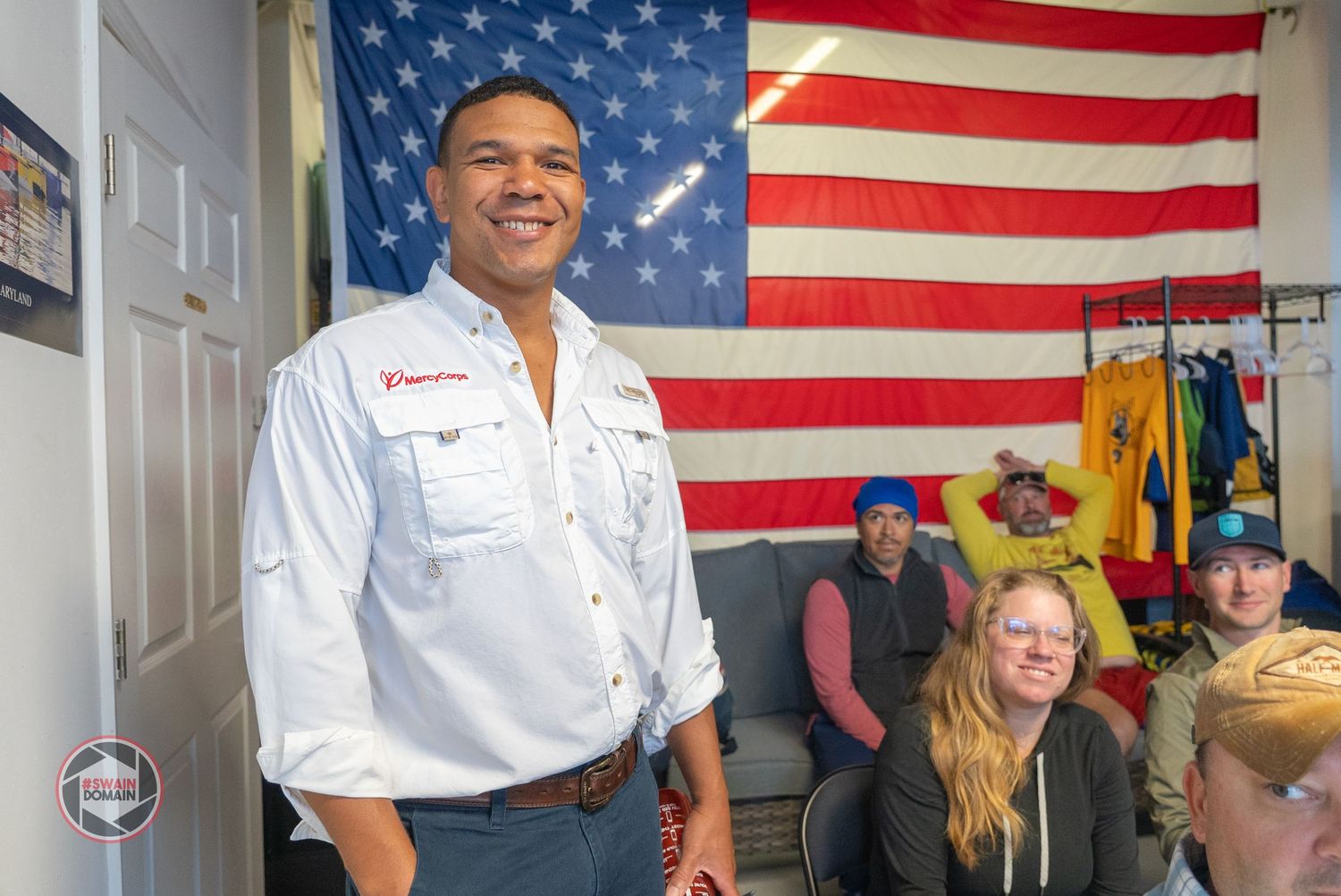 People gather in front of an American flag at a campaign event with patriotic decorations and signage.