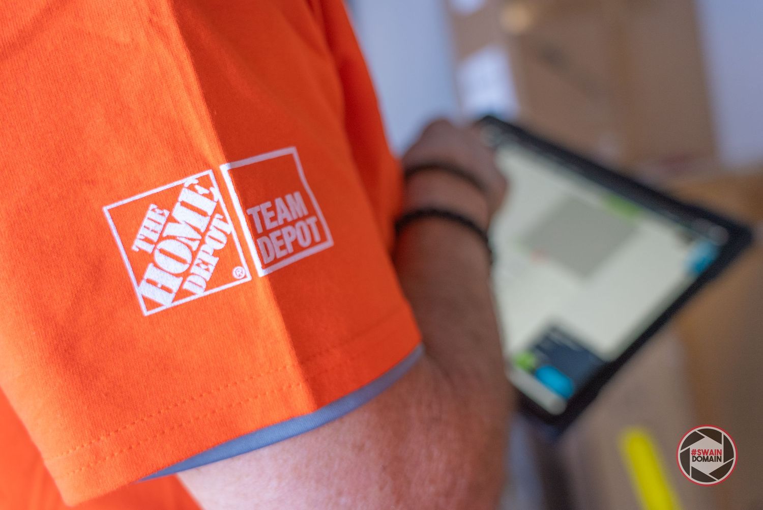 A Home Depot employee in an orange apron assists a customer at the store counter.