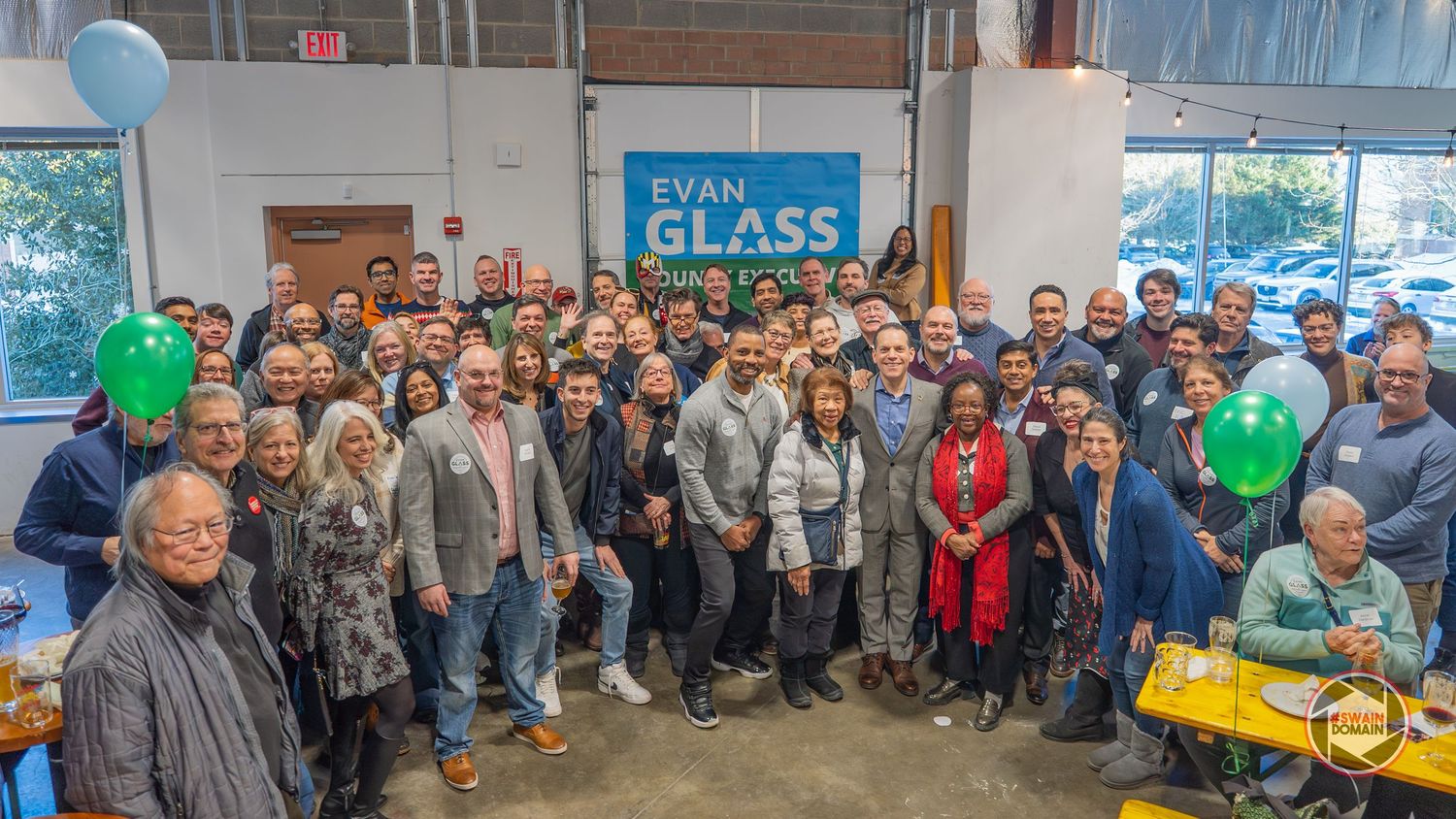 Large group of supporters gather at an Evan Glass campaign event, smiling and posing together indoors.