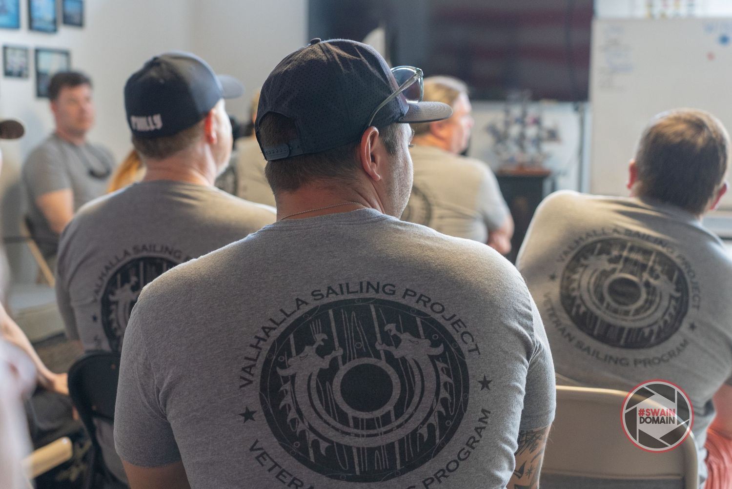 A group of people wearing gray shirts with circular logo designs gather in what appears to be a business setting.