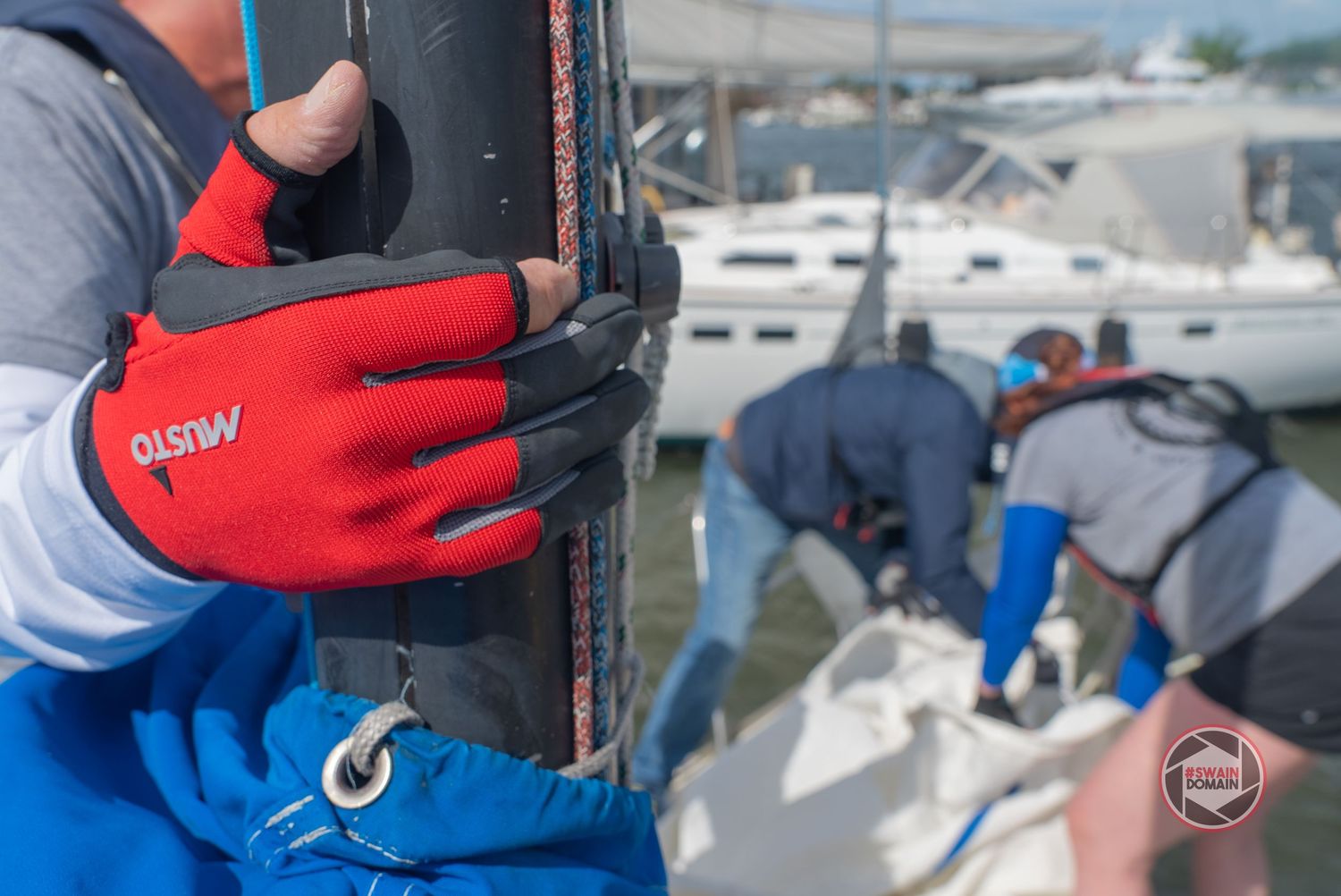 Close-up of hands wearing red work gloves performing maintenance tasks on a boat in a marina.