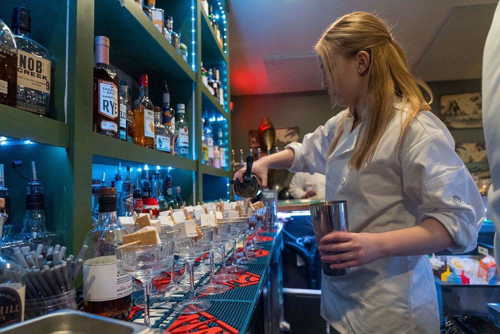 Restaurant staff working behind bar with bottles and glassware.