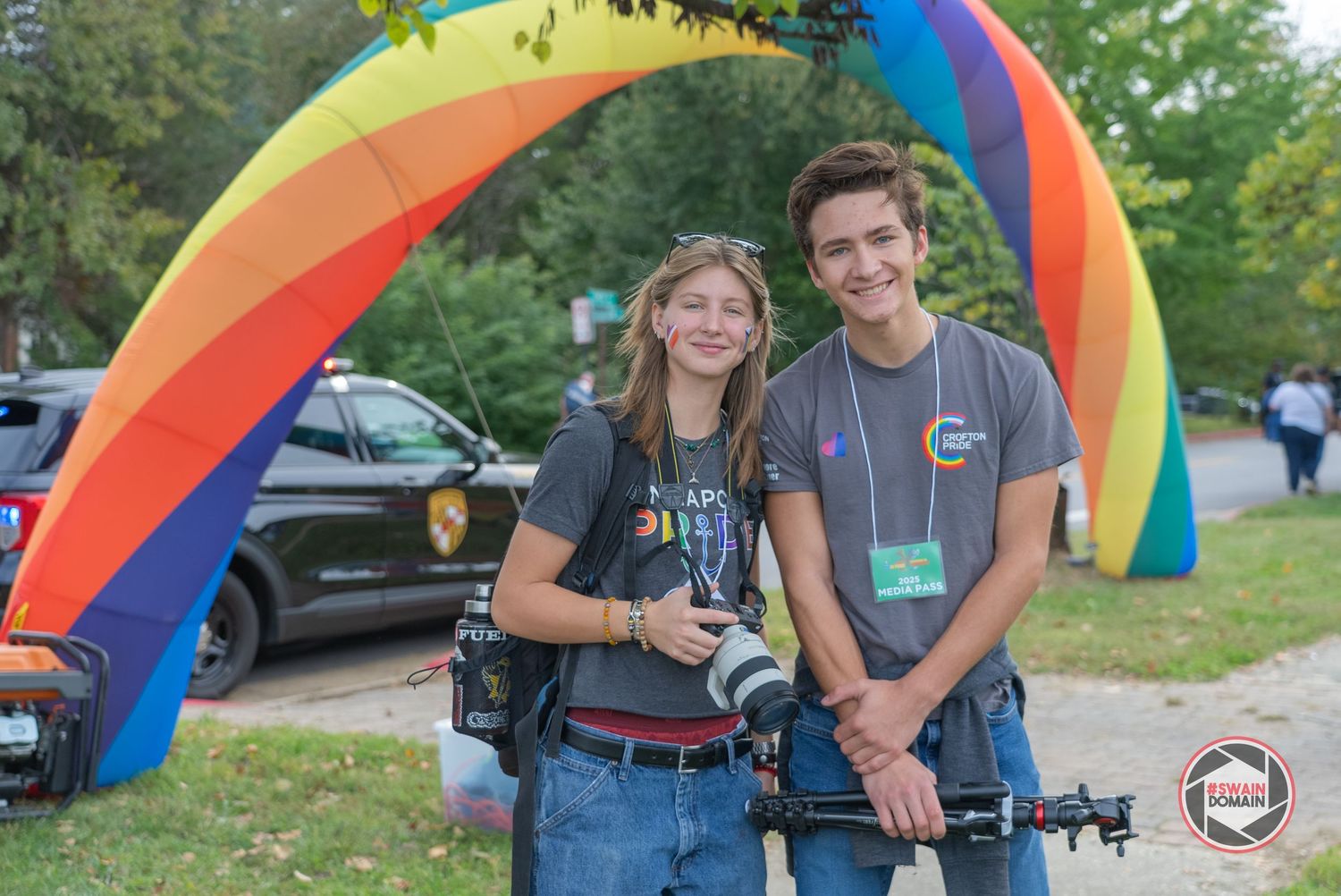 Group of people gathered outdoors near colorful rainbow-themed decorations and equipment.
