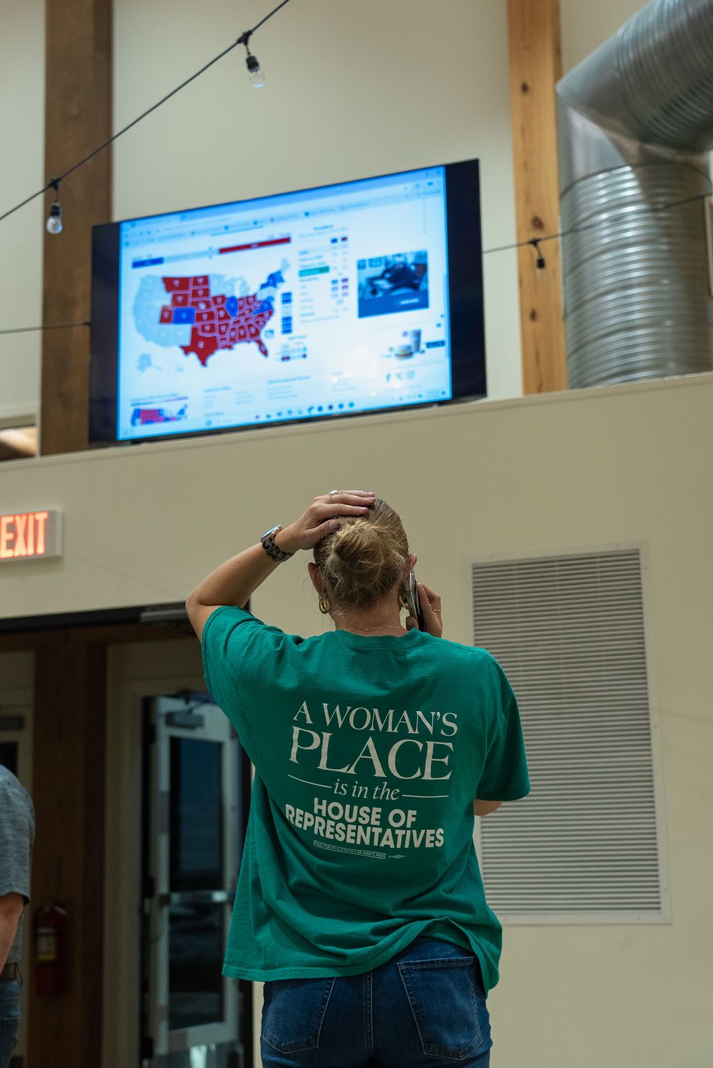 Person wearing green shirt with House of Representatives text in indoor venue.