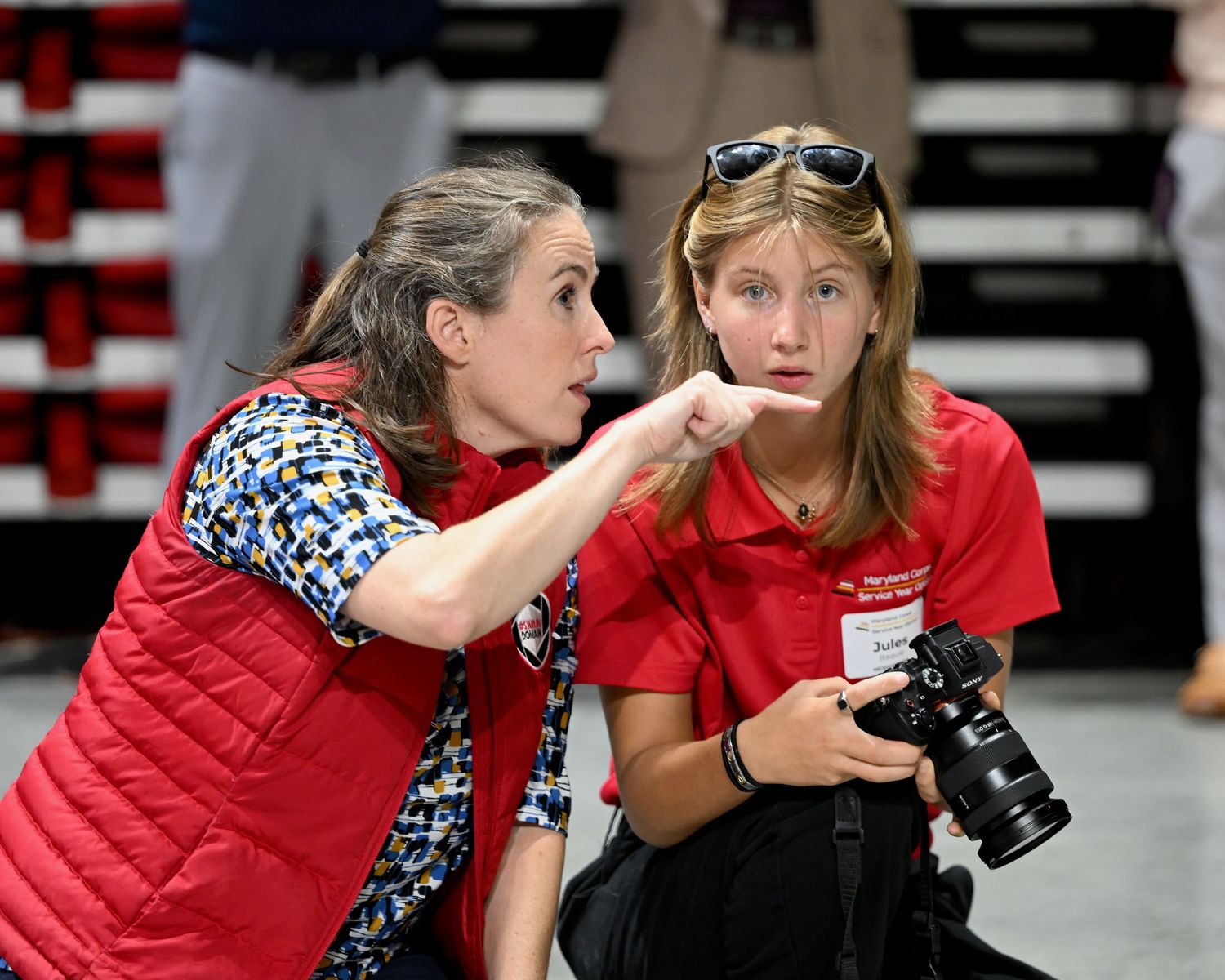 Two people in red and black outfits collaborate while looking at camera equipment.