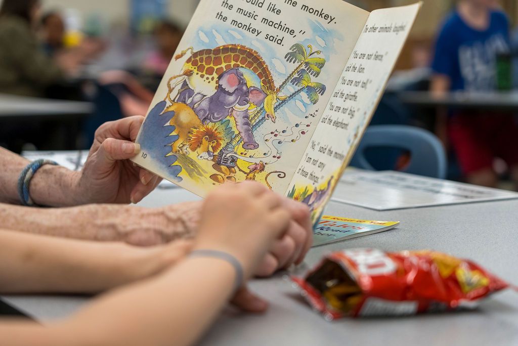 Close-up view of hands holding open children's picture books on a table.