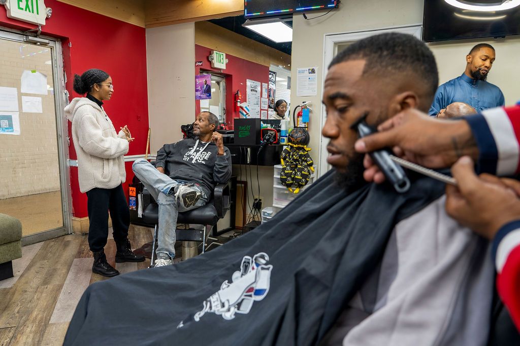 A person receiving a haircut in a barber shop with red walls.