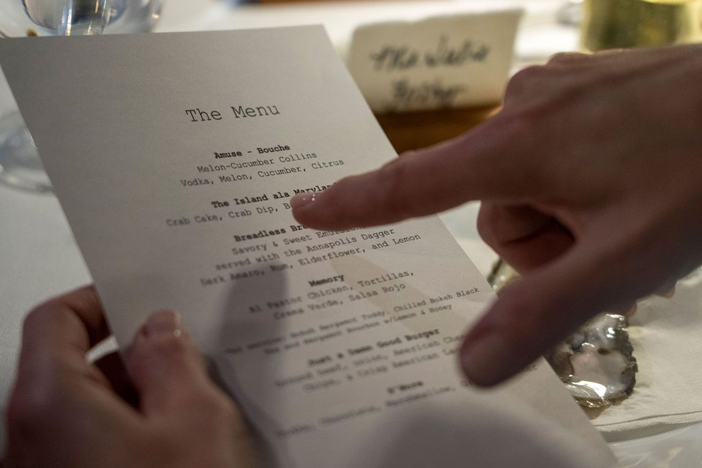 Hand pointing to menu items on an elegant dining table setting.