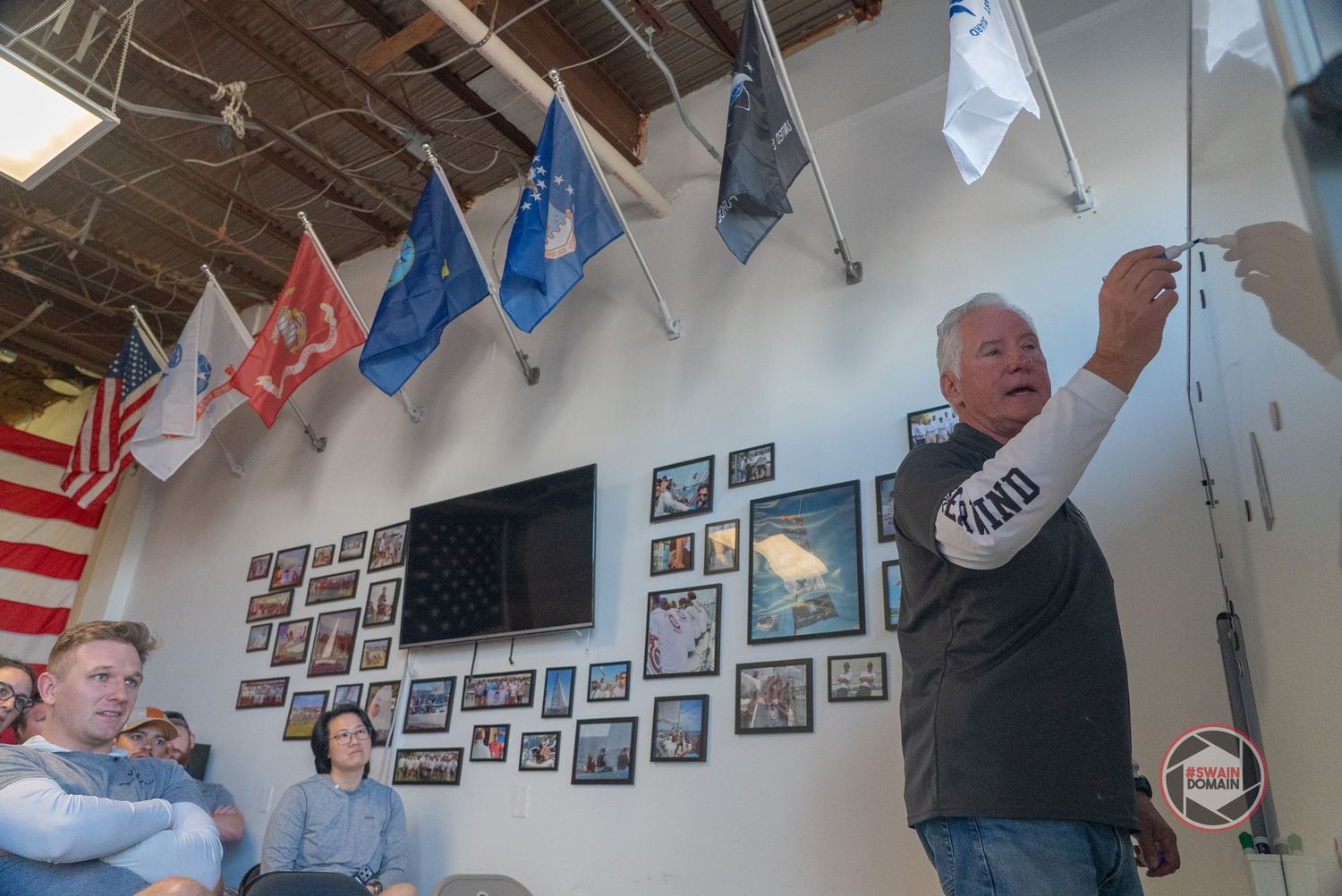 A series of framed photographs displayed along a white wall with colorful flags hanging from the ceiling.