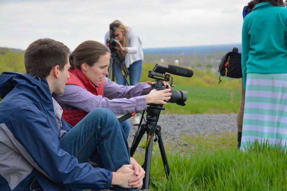 Group of photographers taking pictures outdoors in grassy field with camera equipment.